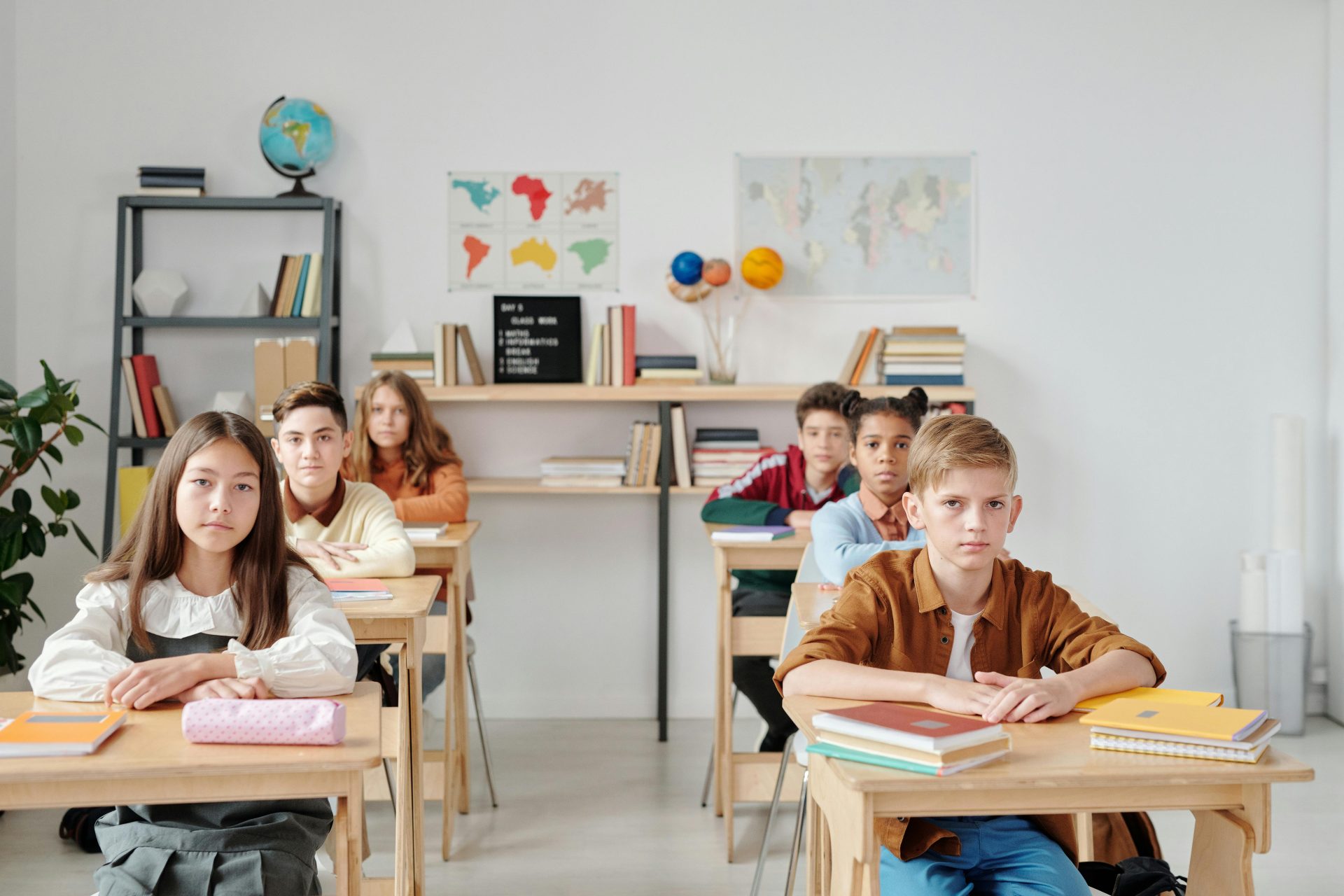 Students sit attentively in a modern classroom with books and maps, focused on learning.